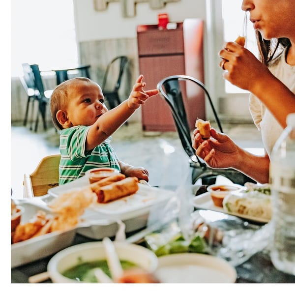 A baby in a high chair reaches for food while a person eats a spring roll at Spring Rollin.