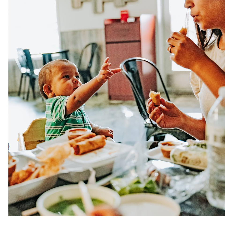 A baby in a high chair reaches for food while a person eats a spring roll at Spring Rollin.