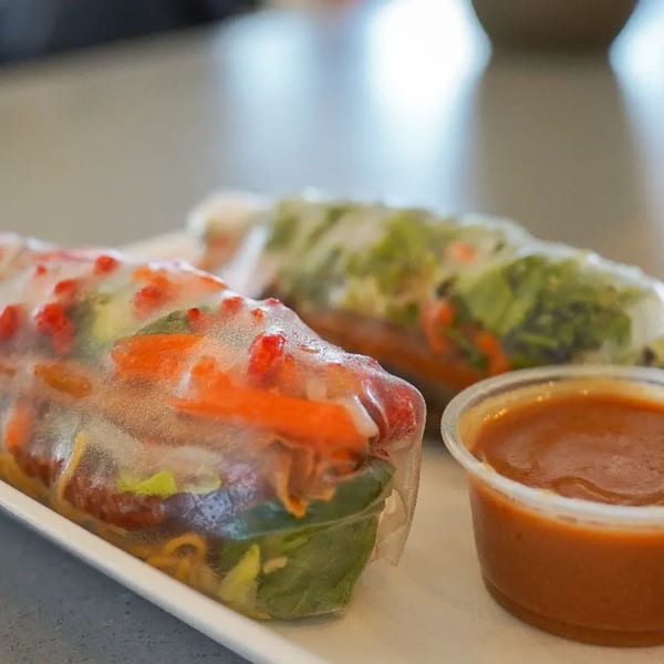 Two fresh Spring Rollin' Vietnamese spring rolls with colorful fillings and a side of dipping sauce.