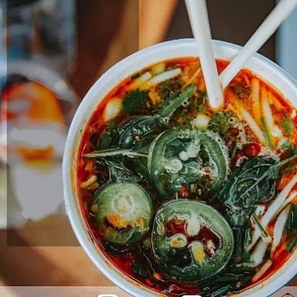 Close-up of a vibrant Vietnamese soup with green vegetables, red broth, and chopsticks.