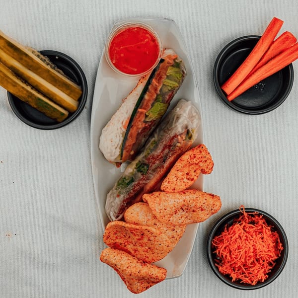 Vietnamese spring rolls, crispy chips, red sauce, pickles, and carrots on a white tablecloth.