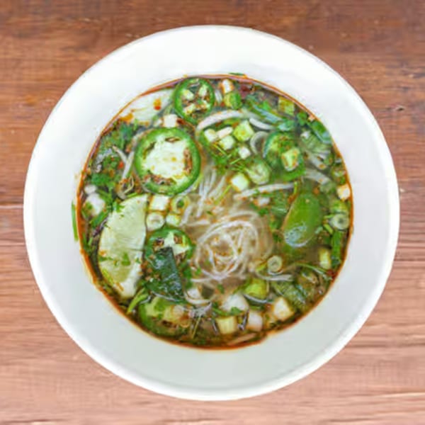 Overhead view of a bowl of Vietnamese pho with noodles, jalapeños, and lime.