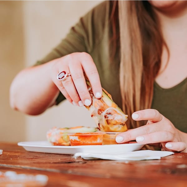 A person dipping a fresh Vietnamese spring roll into a small container of sauce.