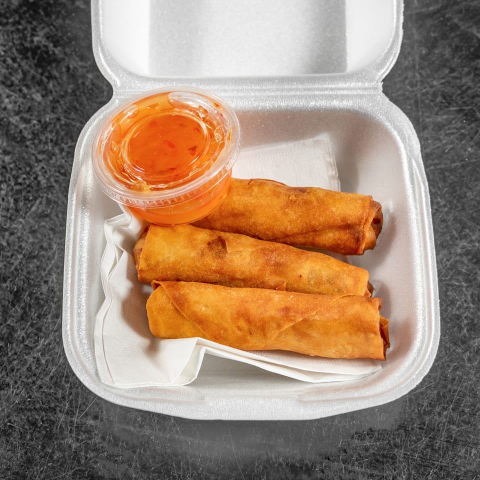 Three golden-brown Spring Rollin' Vietnamese spring rolls and a container of dipping sauce in a takeout box.