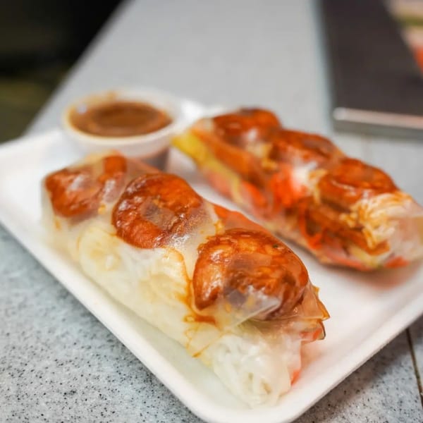 Two Vietnamese spring rolls with shrimp and noodles, served with a side of dipping sauce.
