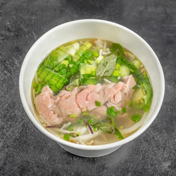A steaming bowl of Vietnamese pho with thinly sliced beef, noodles, and fresh herbs.