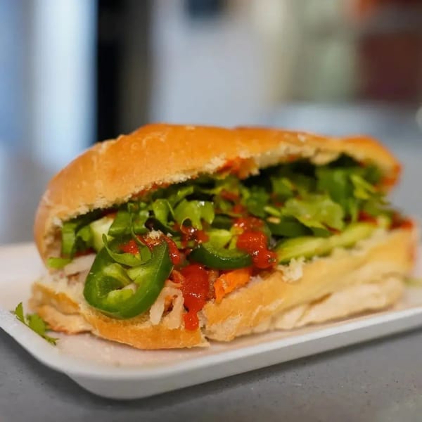 A Vietnamese banh mi sandwich filled with greens, jalapeños, and red sauce on a white plate.