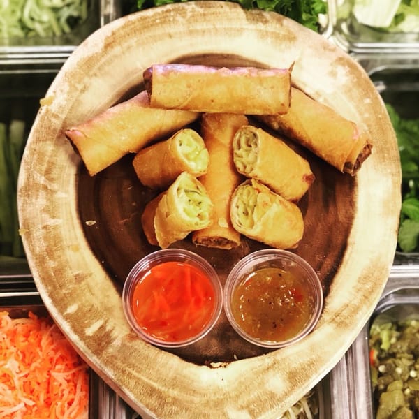Crispy Vietnamese spring rolls, some cut open, with two dipping sauces on a wooden board.