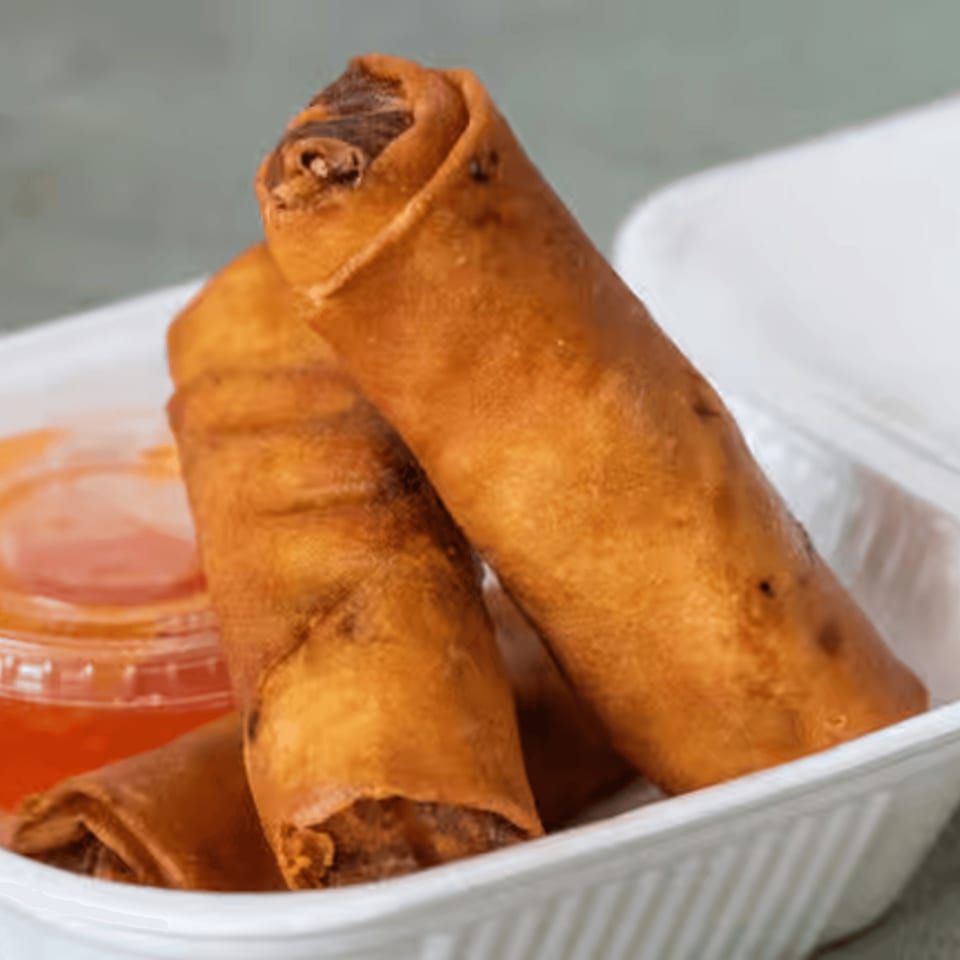 Crispy golden-brown Vietnamese spring rolls in a white takeout container with a side of dipping sauce.
