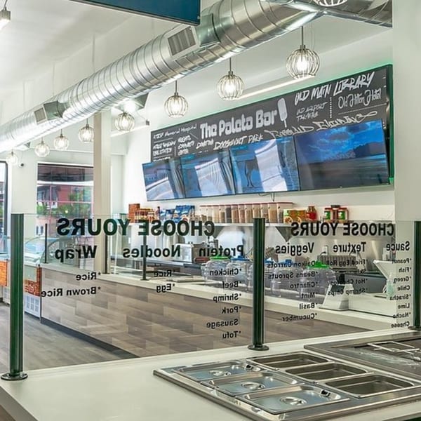 Interior of Spring Rollin, showing a modern, brightly lit counter with a glass sneeze guard and menu.