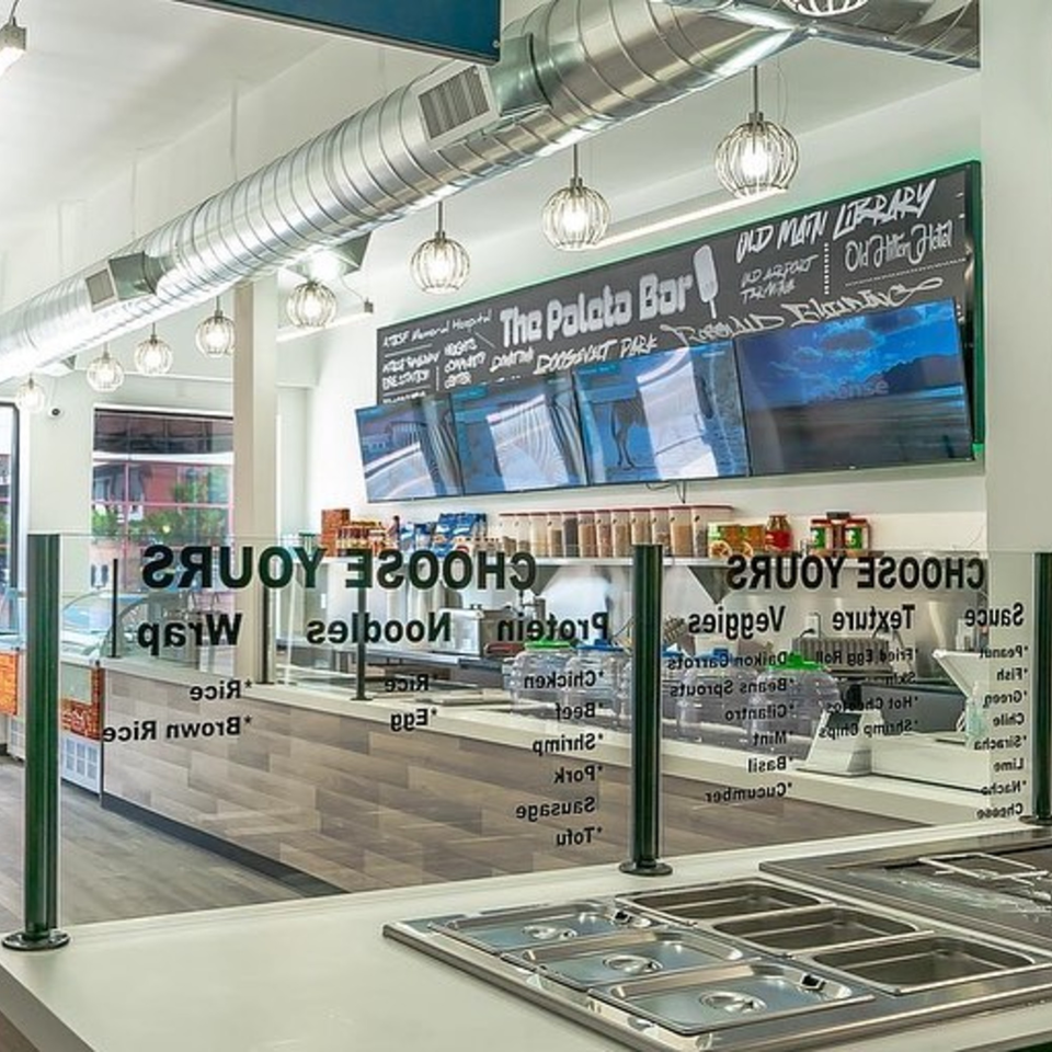 Interior of Spring Rollin, showing a modern, brightly lit counter with a glass sneeze guard and menu.