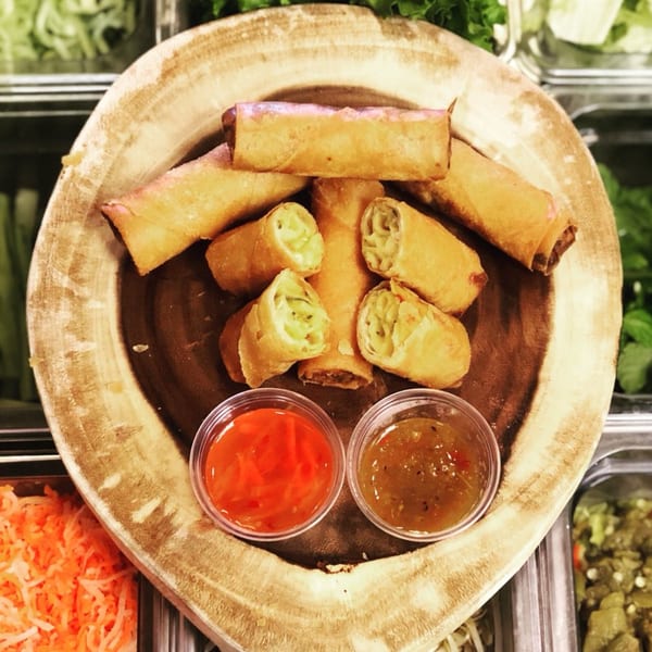 Crispy Vietnamese spring rolls, some cut open, with two dipping sauces on a wooden platter.
