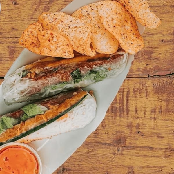 Two Vietnamese spring rolls with crispy chips and a side of orange dipping sauce on wood.