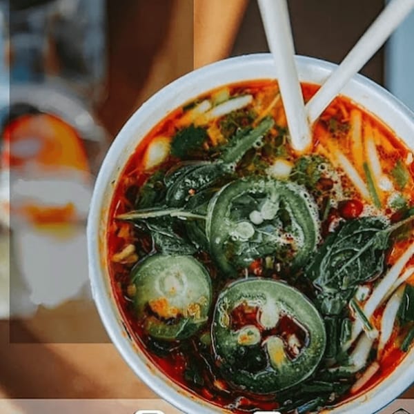 A vibrant Vietnamese soup with green vegetables, red broth, and white chopsticks in a bowl.